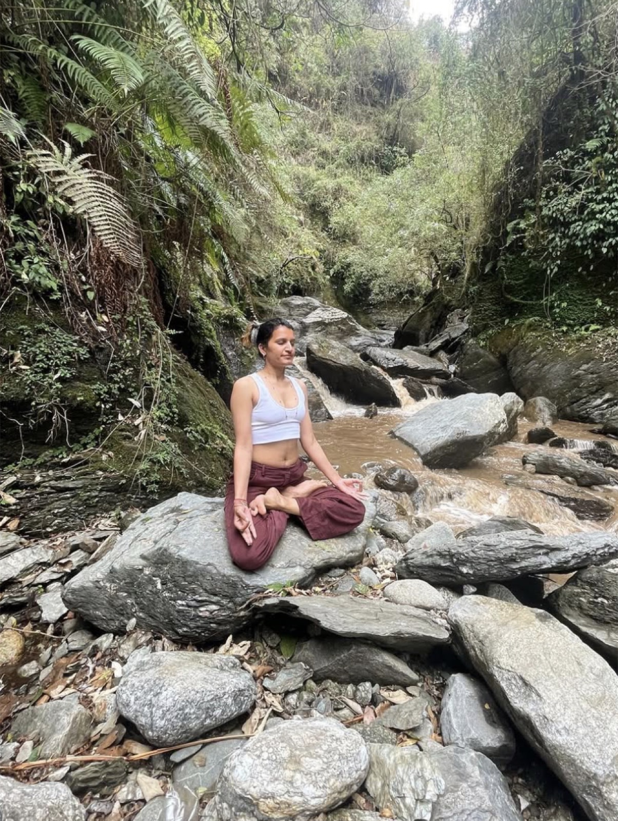 Sameera, yoga teacher and sound healer, meditating beside a rocky stream